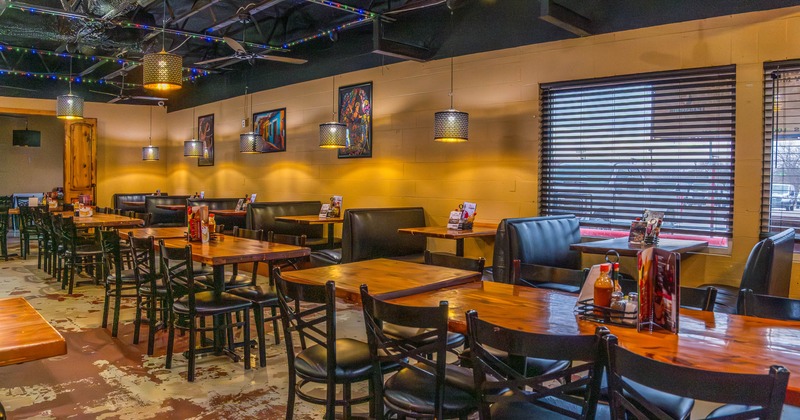 Restaurant interior with wooden tables and chairs, pendant lighting, and booth seating by a window