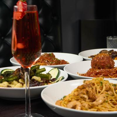 Red cocktail drink with assorted food plates behind it.