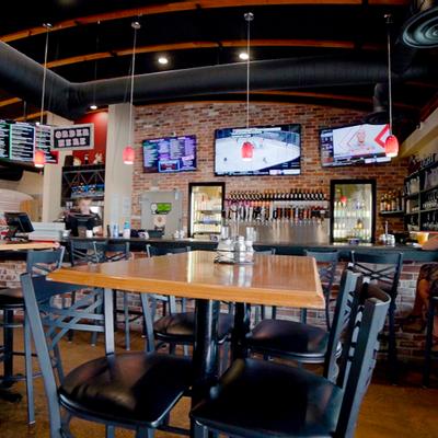 Interior, tall tables and chairs, bar in the back with TVs on the wall