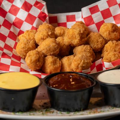 Popcorn chicken on a red and white checkered paper with three dipping sauces.