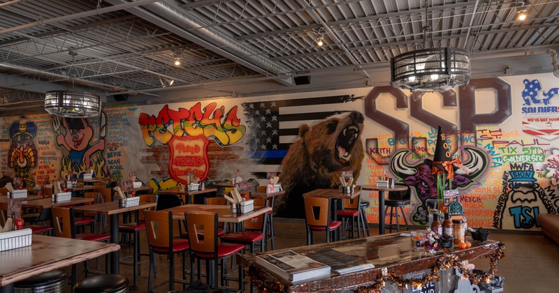 Interior of a colorful restaurant, mural-covered walls, wooden tables