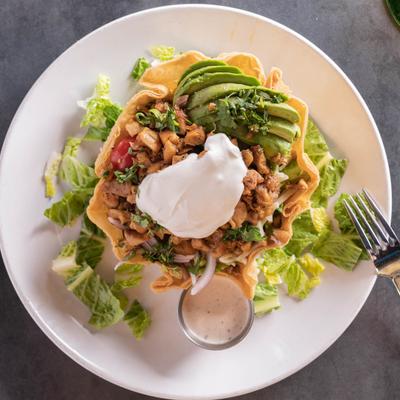 Chicken taco salad, with sour cream, avocado, lettuce, and dressing.