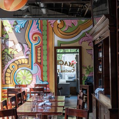 A vibrant restaurant interior with colorful, ornate wall murals and wooden tables set with glasses.