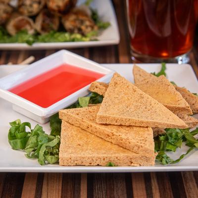Fried tofu triangles with bright red dipping sauce on the side.
