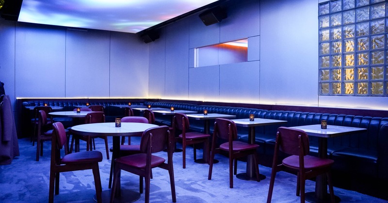 A modern interior - round tables, maroon chairs, a long black banquette under soft lighting