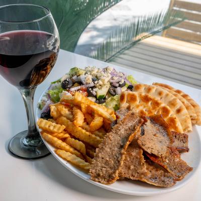 Beef Souvlaki Plate with pita, Greek Salad and fries, paired with a glass of red wine.