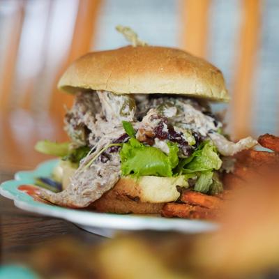 Chicken salad sandwich with lettuce, pecans, and cranberries, served with sweet potato fries.
