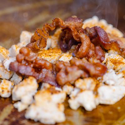 Chicken pieces and bacon being cooked on a flat-top griddle.