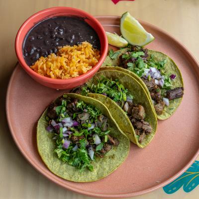 Chorizo tacos topped with onion and cilantro, served with black beans and lime wedges.