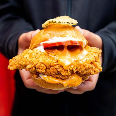 Hands holding a chicken slider with cheese and a tomato slice.
