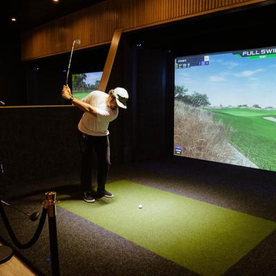 Indoor golf simulator with a person taking a swing in front of a group of people.