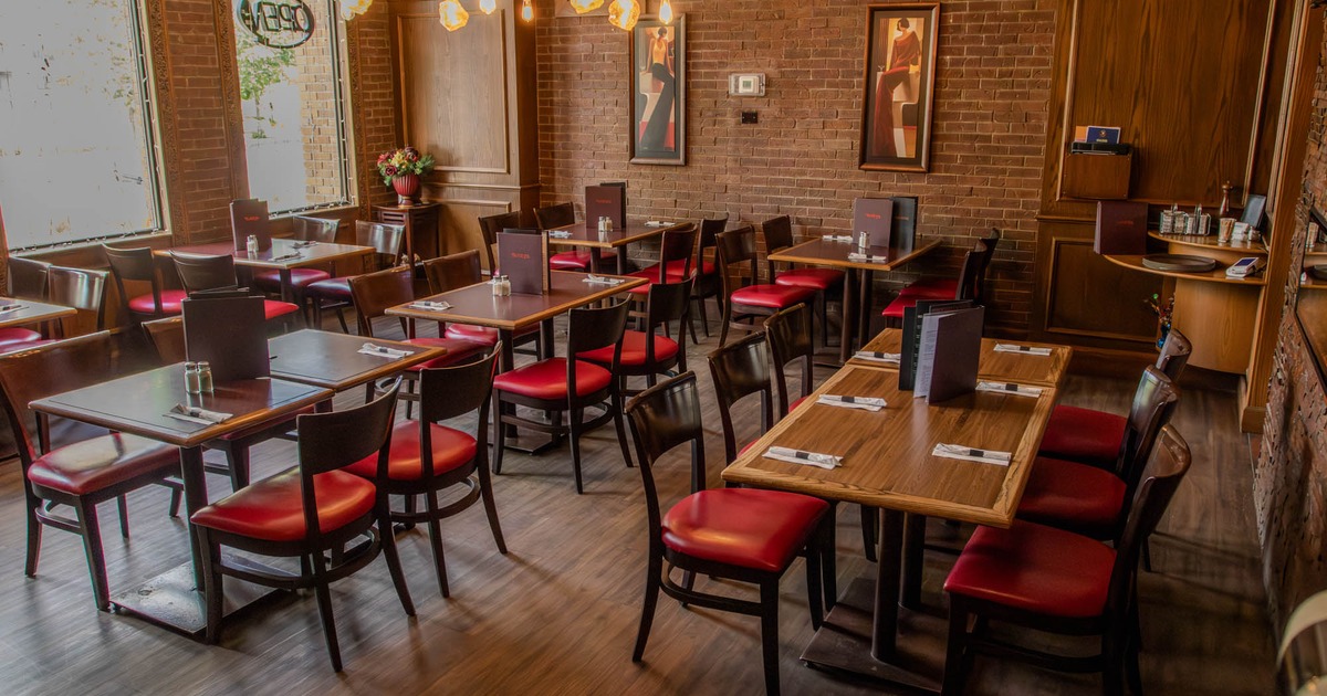Restaurant interior with wooden tables, red cushioned chairs, brick walls
