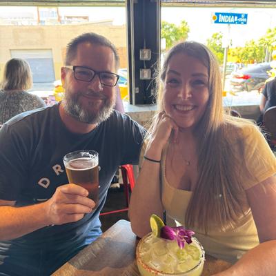 Beautiful Couple Smiling, man is holding a beer, a margarita sits on their table.