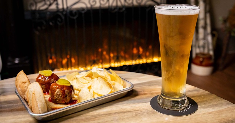 A table by fireplace with glass of beer and dish on it.