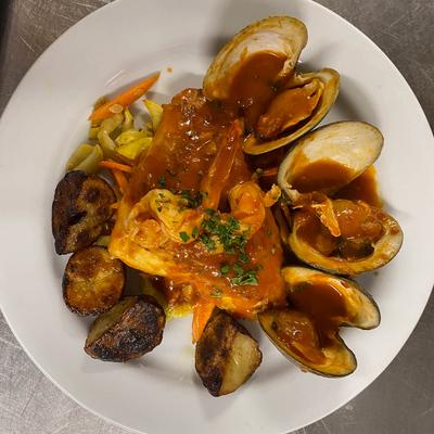 A plate of clams with shrimp, roasted potatoes, sauteed vegetables, and rich sauce.