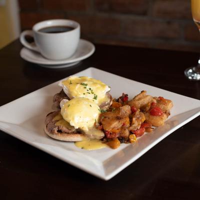Eggs Benedict with cooked potatoes and peppers on the side.