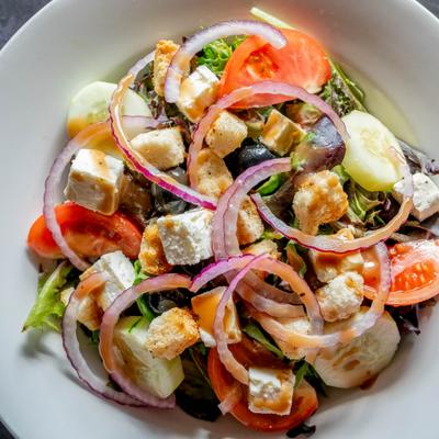 Mediterranean salad with tomatoes, cucumbers, red onion rings, feta cheese cubes, and olives.