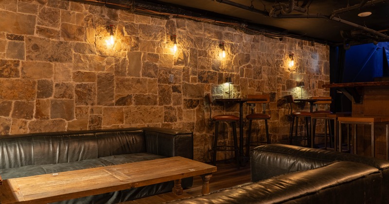 Dimly lit lounge with stone walls, leather couches, and wooden tables