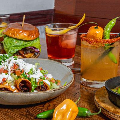 Multiple food plates and cocktails. Flautas, margaritas, negroni, mexican candy shot, and a double angus cheeseburger.