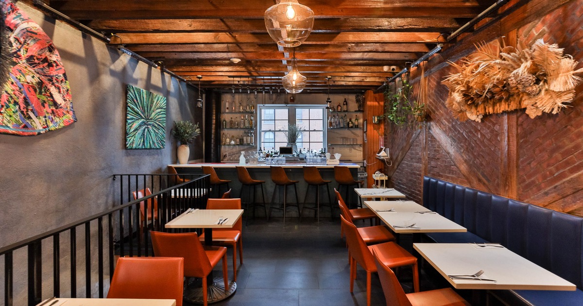 Interior with tables, orange chairs, a bar with stools, and exposed wooden beams on the ceiling.