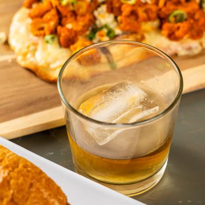 Whiskey on the rocks with a chicken flatbread in the background.