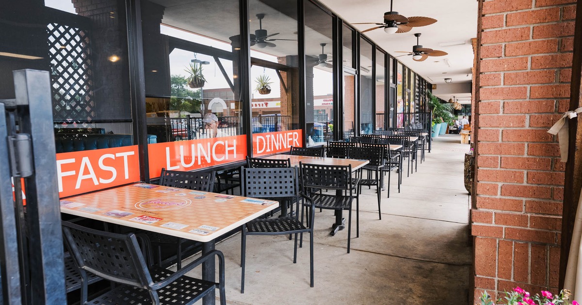 Outdoor dining area with tables, chairs, and ceiling fans under an awning