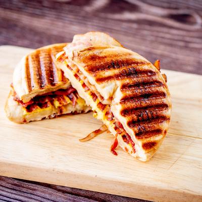 Grilled panini with melted cheese and bacon on a wooden board.