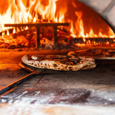 Two pizzas cooking inside a wood-fired oven with visible flames.
