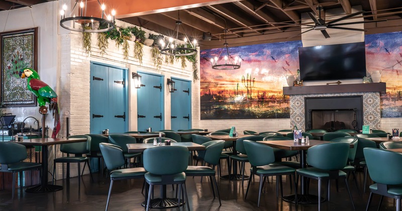 Interior, teal chairs, wooden tables, blue doors, a desert sunset mural, and a tiled fireplace