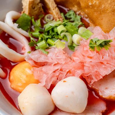 Thai pink noodle soup featuring savory fermented bean broth and mixed seafood toppings.