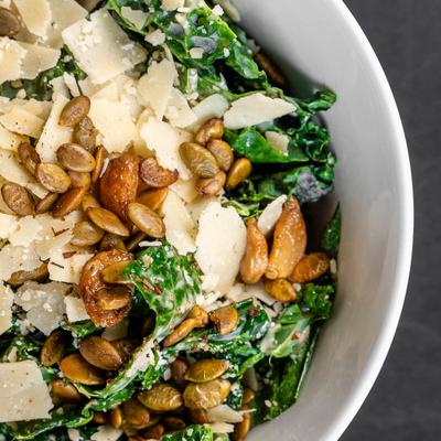 A kale salad with shaved parmesan, almonds, and pepitas, close-up.