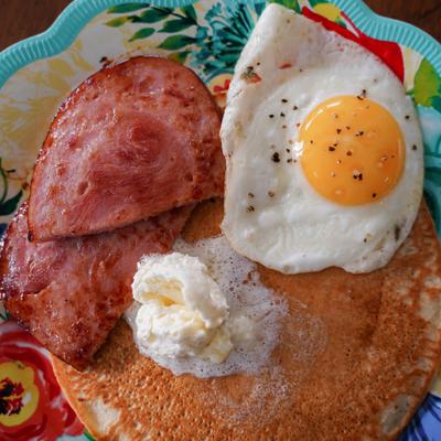 Pancakes topped with a fried egg, butter, and two slices of ham.