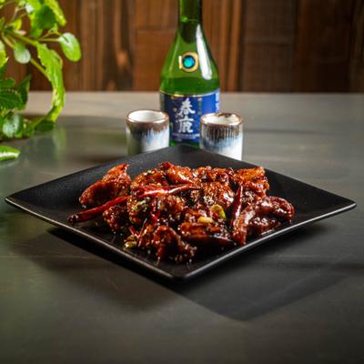 Spicy chicken wings on a black plate, accompanied by cups of sake.