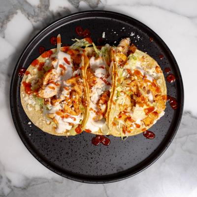 Buffalo chicken tacos topped with sauces and crumbled cheese.