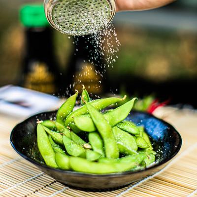 Sprinkling salt on edamame bowl on the table outside, close up