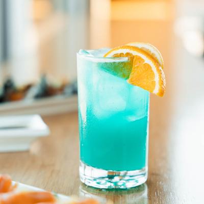 A light blue cocktail garnished with an orange wedge.