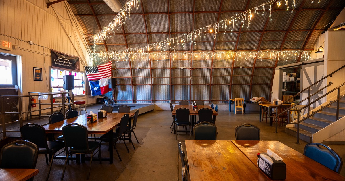 A rustic event space with wooden tables, chairs, and string lights