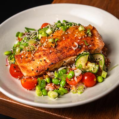 Seared salmon served over rice, edamame, cherry tomatoes, chopped scallions, and cucumbers..