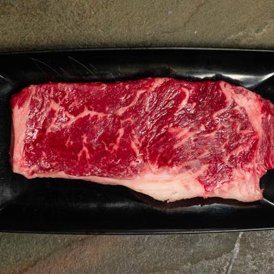 Ribeye steak raw cut on a black plate.