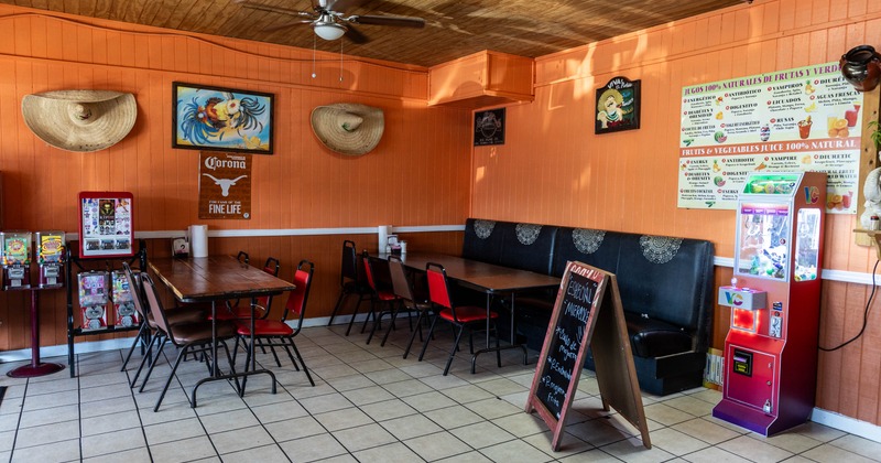 Interior of a casual restaurant with orange walls, wooden ceiling, tables, chairs, straw hats