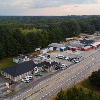 Aerial view of roadside buildings and a parking lot surrounded by green trees.