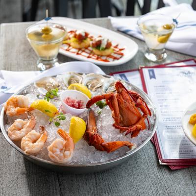Chilled seafood platter served on the table alogside coupl of cocktails and a appetizer.