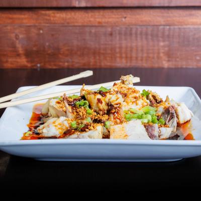 Spicy chicken with chili oil, crushed peanuts, scallions, and chopsticks on a white plate.