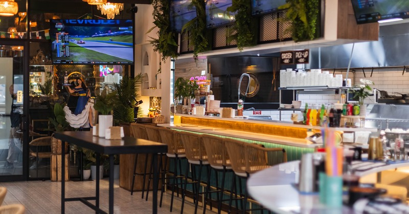 A modern bar - a long counter, high stools, TVs, warm lighting and decorative plants