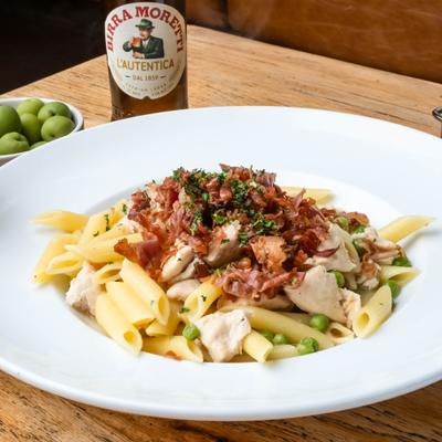 Pasta with crispy proscuitto, peas and chicken, alongside bottle of beef and bowl with olives.