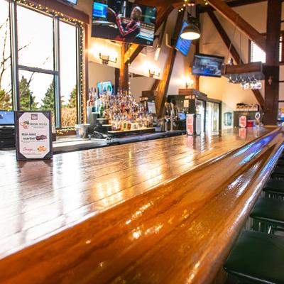 Bar area with a wooden counter top, fully stocked bar and televisions.