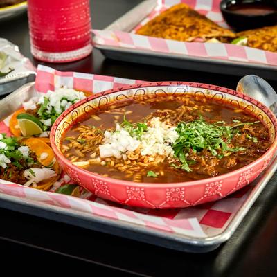 A bowl of birria ramen with cilantro and onions served with tacos on a tray.