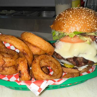 Cheeseburger with onion rings in a green basket on checkered paper.