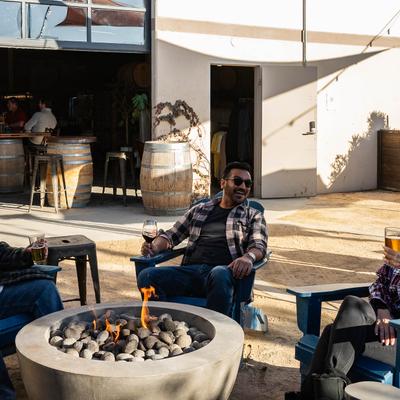 Outside seating, people having drinks around a modern fire pit on a sunny day.