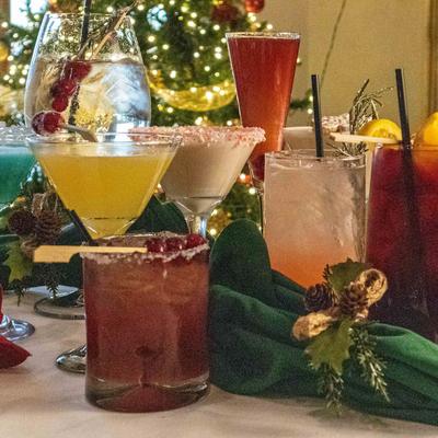 Festive cocktails in various colors on a table with green napkins and Christmas decor.